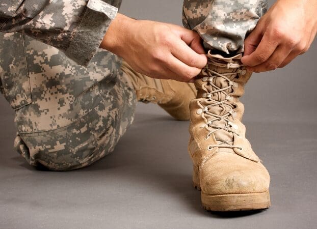 Military person tying boot laces close-up.